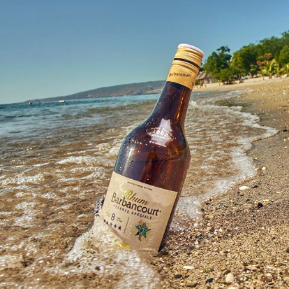 Eine Flasche Barbancourt wird am Strand von einer Welle umspült
