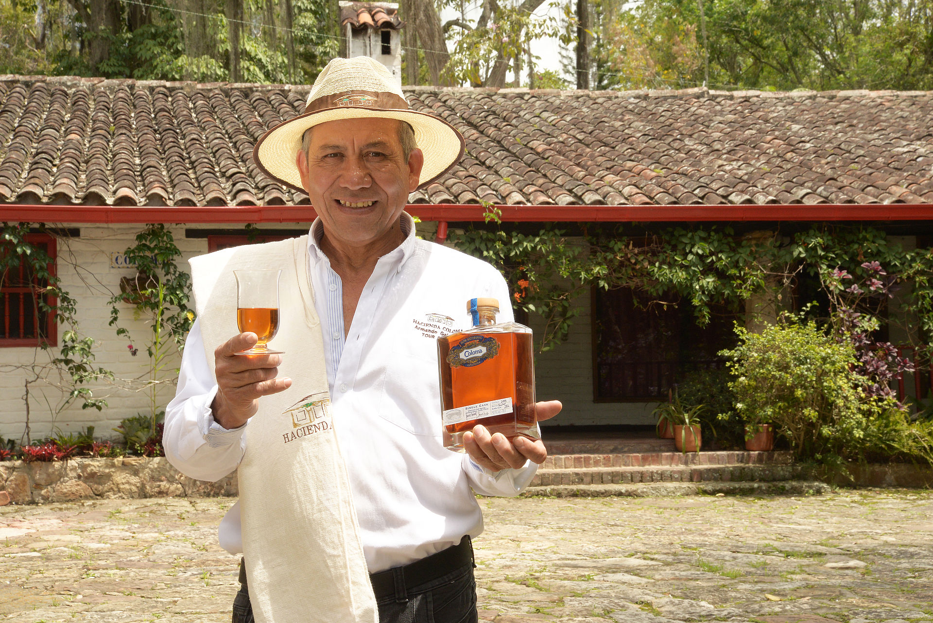 Mann in traditioneller Kleidung hält eine Flasche Coloma und ein gefülltes Glas in den Händen